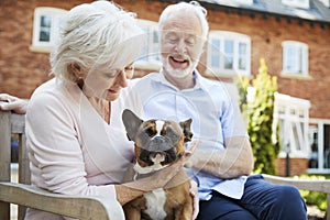 Retired Couple Sitting On Bench With Pet French Bulldog In Assisted Living Facility