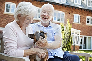 Retired Couple Sitting On Bench With Pet French Bulldog In Assisted Living Facility