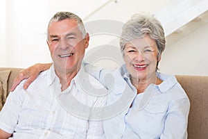 Retired couple sitting on couch smiling at camera