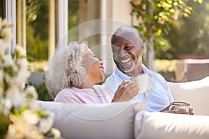 Retired Couple Sitting Outdoors At Home Having Morning Coffee Together