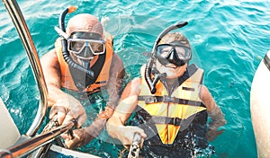 Retired couple taking happy selfie in tropical sea excursion with life vests and snorkel masks - Boat trip snorkeling