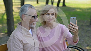 Retired couple taking selfie photo by smartphone in park, vacation memories