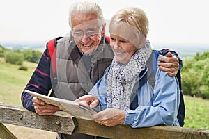 Retired Couple On Walking Holiday Resting On Gate With Map