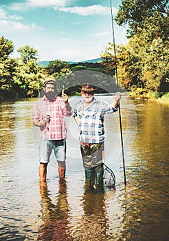 Retired dad and mature bearded son. Happy bearded fishers in water. Men relaxing nature background. Brutal man stand in