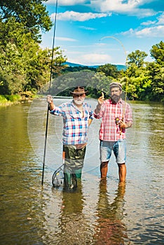 Retired dad and mature bearded son. Happy bearded fishers in water. Men relaxing nature background. Brutal man stand in