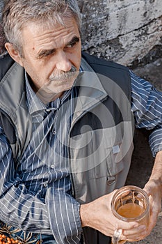 Retired elderly man sits on concrete staircase, drinks beer and thinks about his problems