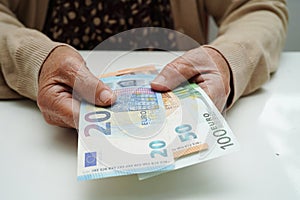 Retired elderly woman holding Euro banknotes money and worry about monthly expenses and treatment fee payment