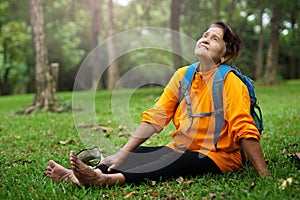 Happy senior lady sitting on green grass at park.