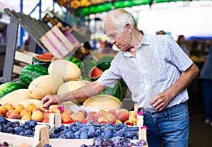 Retired european man buying plums peaches nectarine in market