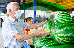 Retired european man wearing medical mask protecting against the virus buying melons and watermelons in market