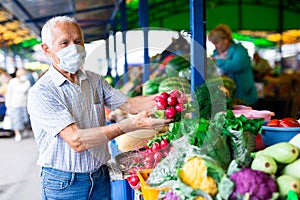 Retired european man wearing medical mask protecting against the virus buying radishes and cabbage in market