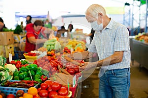 Retired european man wearing medical mask protecting against virus buying tomatoes in market