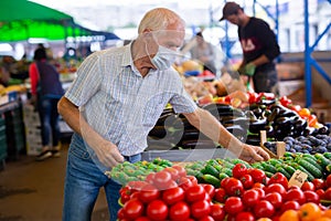 Retired european man wearing medical mask protecting against virus buying tomatoes in market