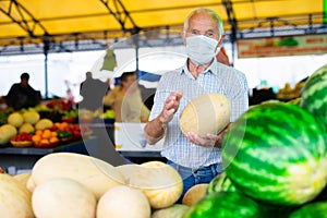 Retired european man wearing medical mask protecting against the virus selling melons and watermelons in market