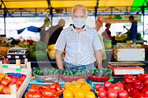 Retired european man wearing medical mask protecting against virus selling vegetables in market