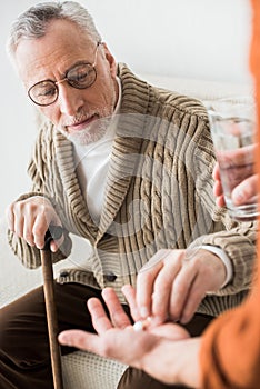 Retired father taking pills from hand of son holding glass of water