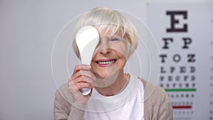 Retired female closing eye and smiling to camera, successful cataract surgery