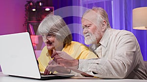 retired gamers, modern elderly man and woman having fun playing computer games on a laptop while sitting at a table in