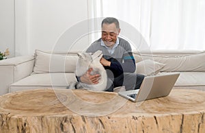 Retired grandfather spending time with his pet in living room at home. Laptop computer are on a table made from large tree trunk
