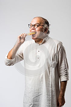 Retired Indian old man eating ice cream, standing icolated against white background