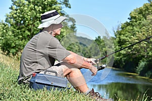 Retired Male Fisherman Sitting With Fishing Rod Outdoors