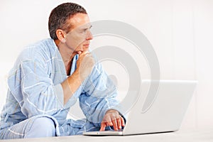 Retired man in bathrobe with laptop looking at copyspace. Portrait of a retired man in bathrobe with laptop looking at