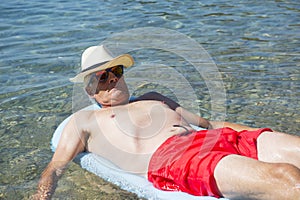 Retired man floating on bed in sea water