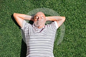 Retired man lying on his back on grass with hands on head with grass background.