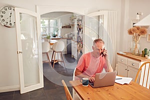 Retired Man On Phone At Home In Kitchen Using Laptop