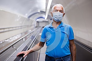 Retired man in protective mask walking down the escalator to metro station