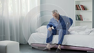 Retired man sitting in bed and feeling terrible pain in back, health and illness