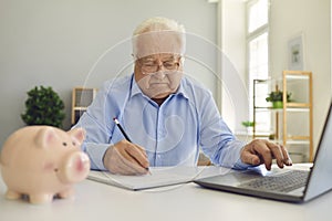 Retired man using laptop and taking notes in notebook studying pension plan and managing his budget