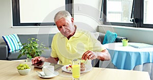 Retired man using tablet while eating breakfast