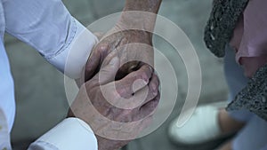 Retired man with walking stick moving in park, caring wife covering husband hand