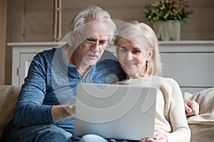 Retired old couple using laptop together talking sitting on sofa