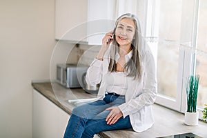 Retired people and technologies. Pleasant cheerful senior gray haired woman in white shirt and denim, talking on cell