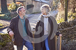 Retired Senior Couple Opening Gate On Winter Walk Through Village In Countryside Together