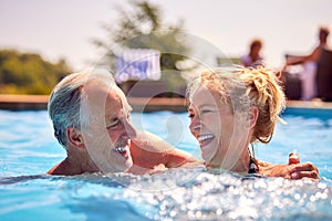 Retired Senior Couple Relaxing In Swimming Pool On Summer Vacation