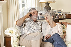 Retired Senior Couple Sitting On Sofa Talking On Phone At Home Together