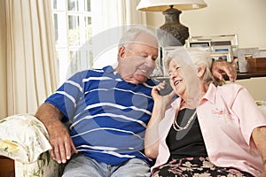 Retired Senior Couple Sitting On Sofa Talking On Phone At Home Together