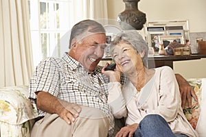 Retired Senior Couple Sitting On Sofa Talking On Phone At Home Together