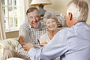 Retired Senior Couple Sitting On Sofa Talking To Financial Advisor