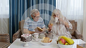 Retired senior couple talking drinking tea, reading book in modern living home room lounge together