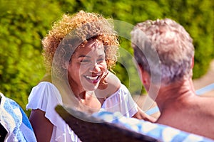 Retired Senior Couple Talking On Loungers Relaxing By Swimming Pool On Summer Vacation