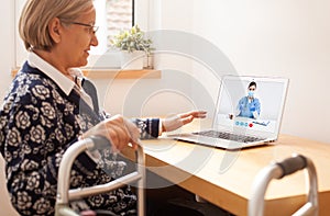 Retired senior elderly woman with mobility problem talking to UK NHS GP female doctor via virtual telemedicine video call