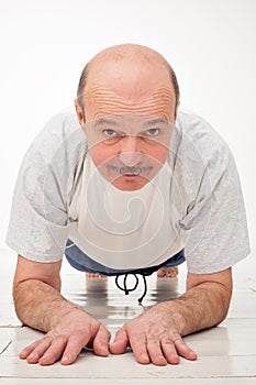 Retired senior man on abdominals workout doing basic plank