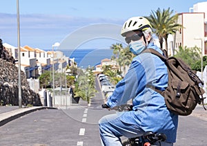 Retired senior man in deserted road with bicycle and yellow helmet wearing face mask due to coronavirus. Blue sky and horizon over