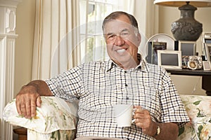 Retired Senior Man Sitting On Sofa Drinking Tea At Home