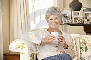 Retired Senior Woman Sitting On Sofa Drinking Tea At Home