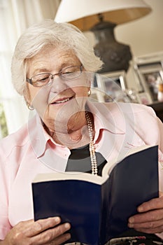 Retired Senior Woman Sitting On Sofa At Home Reading Book